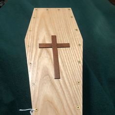 a wooden box with a cross on the top and string attached to it, sitting on a green cloth