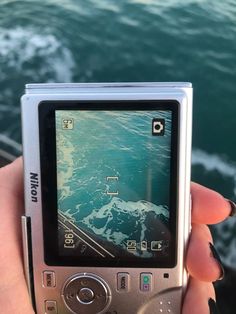 a person holding up a cell phone in front of the camera with water behind them