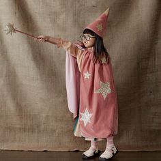 The combination of luxurious pink velvet, with gold glitter fabric stars and moons, makes this costume very special. Simply wrap around the cape, pop on the hat, and wave the star topped wand, to look like a wizard in seconds. It's perfect to wear to parties, or for imaginative play. Pink velvet cape, with gold glitter fabric moons and stars, with a cotton lining and a snap fastening at the neck. Pink velvet hat, with gold glitter fabric moons and stars The wand is topped with a gold glitter fab Pink Fantasy Costume For Party, Pink Fantasy Costume For Costume Party, Pink Fantasy Costume For Fantasy Events, Wizard Costume, Star Costume, Stars And Moons, Velvet Cape, Dress Up Boxes, Diy Bebe