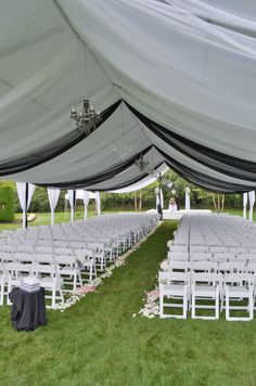 an outdoor wedding setup with white chairs and black tablecloths on the grass under a tent