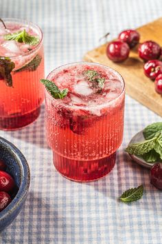 two glasses filled with ice and cherries on top of a table