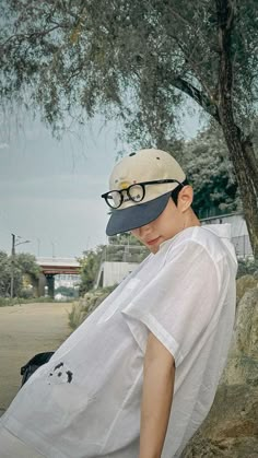 a boy wearing glasses and a hat leaning against a tree