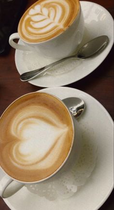 two white plates topped with cups and saucers filled with coffee latte art designs