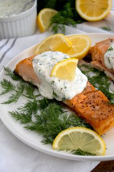 two salmon fillets on a white plate with lemons and dill garnish