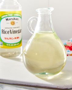 a bottle of rice vinegar next to an empty glass jug on a tray with other ingredients