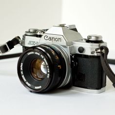 a canon camera sitting on top of a white table next to a black and silver strap