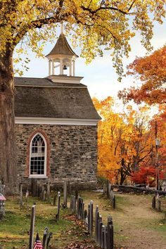 an old stone church surrounded by trees with autumn leaves on the ground and in front