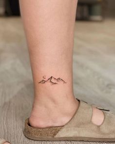 a woman's foot with a small mountain tattoo on the side of her leg