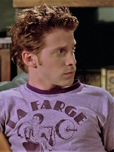 the young man is wearing a purple shirt and looking off to his left with an intense look on his face