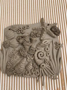 an intricately designed clay sculpture on a striped surface with shells and seaweeds