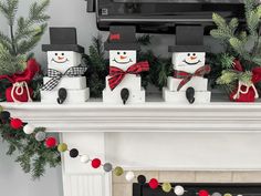 three snowmen are sitting in front of a fireplace decorated with christmas garland and pom poms