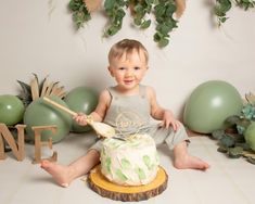 a baby sitting on the floor with a cake in front of him and some balloons