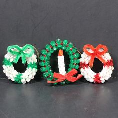 three small christmas wreaths made out of beads and bows on a black table top