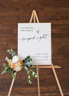 an easel with flowers and greenery on it in front of a wooden wall