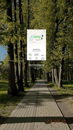 a wooden walkway in the middle of a park with trees on both sides and a sign above it