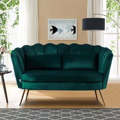 a green couch sitting in front of a window next to a table with a lamp on it