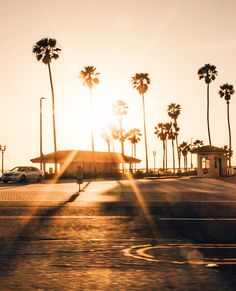 the sun shines brightly through palm trees in an empty parking lot