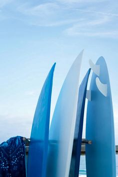 three surfboards leaning against each other in front of the ocean on a sunny day