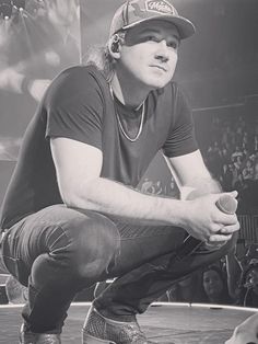 a black and white photo of a man in a baseball cap sitting on a stage