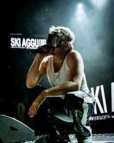 a man sitting on top of a stage holding a microphone to his ear while wearing ski goggles