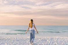 a woman walking on the beach with her arms outstretched