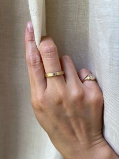 a woman's hand with a gold ring on her finger and a white curtain in the background