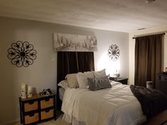 a bedroom with white bedding and brown drapes on the window sill, two nightstands are also decorated with decorative wall art