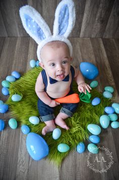 a baby wearing bunny ears and holding an orange carrot in front of some blue eggs