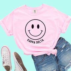 a pink t - shirt that says ketta tau alpla with a smiley face on it