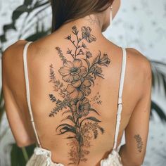 the back of a woman's neck with flowers and leaves tattooed on her lower back