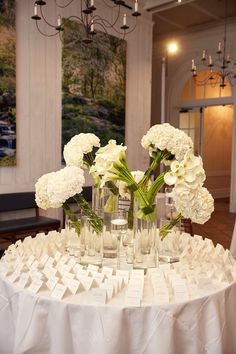 white flowers in vases on top of a round table with place cards and napkins