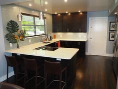 a kitchen with black cabinets and white counter tops, dark wood flooring and bar stools