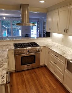 a kitchen with white cabinets and marble counter tops, stainless steel oven hood over the stove