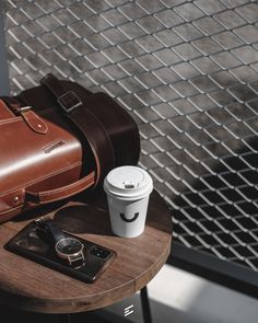 a table with a coffee cup, cell phone and bag on it next to a fence