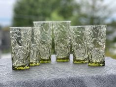 four glasses sitting on top of a table next to each other with trees in the background