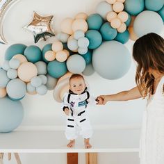 a woman is holding the hand of a baby in an astronaut suit while standing on a table