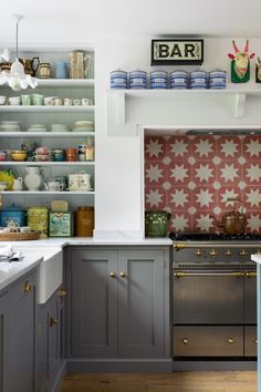 a kitchen with gray cabinets and white counter tops, an oven and shelves filled with dishes