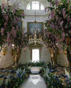 an indoor ceremony with purple flowers and greenery on the ceiling, chandelier hanging from the ceiling