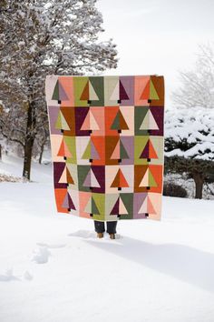 a person standing in the snow with a quilt on it's back and trees in the background