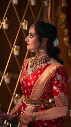 a woman in a red and gold sari with jewelry on her neck standing next to candles