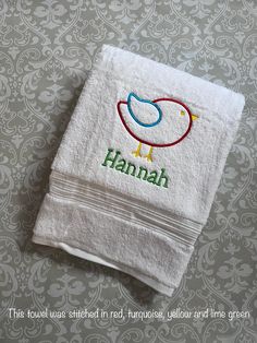 a white towel with the word hannah on it and a bird embroidered onto it, sitting on a patterned wallpapered surface