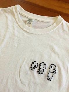 an embroidered t - shirt with three little aliens on it