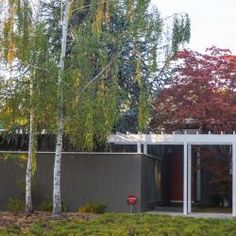 a house with trees in the front yard and bushes on the other side of it