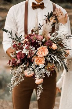 a man holding a bouquet of flowers and greenery in his hands while standing next to a woman