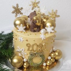 a christmas cake with gold decorations and a teddy bear sitting on top, surrounded by greenery