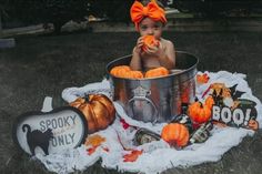 a baby sitting in a metal tub with pumpkins and booze on the ground