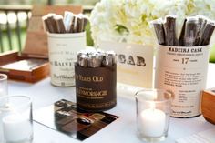 a table topped with bottles and candles on top of a white table cloth next to flowers