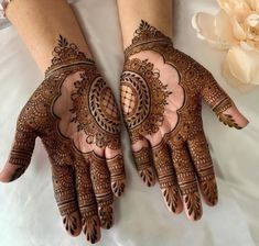 two hands with henna designs on them, one is holding a flower and the other has