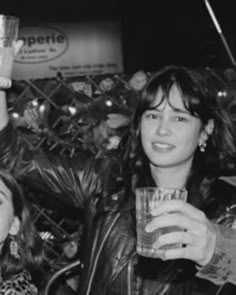 black and white photograph of two women holding up drinks in front of a fenced area