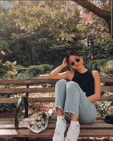 a woman sitting on top of a wooden bench next to a flower pot and sunglasses